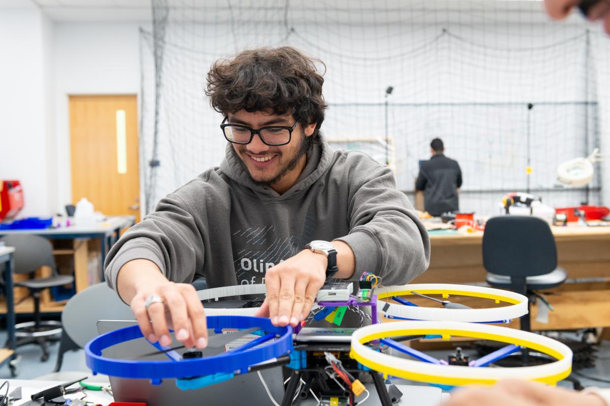A robotics student smiles while adjusting a piece of a machine.