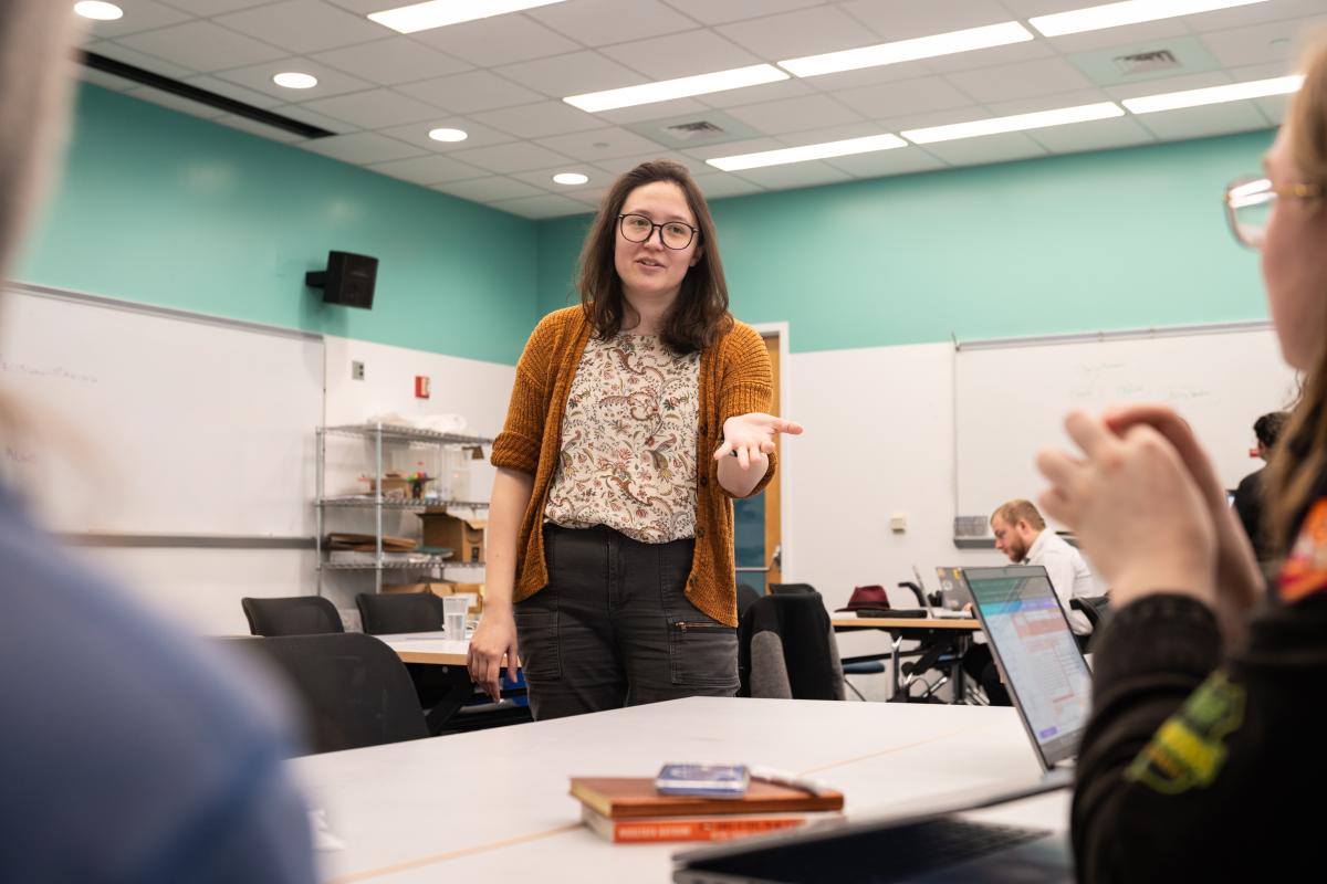A photo of Professor Victoria Preston standing behind a table while instructing a pair of Probalistic Robotics students