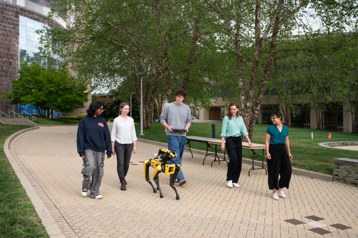 Olin Students and Faculty walk through campus with a four-legged robot,