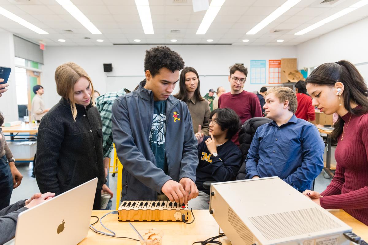 A group of Olin College of Engineering students gather around a made-from-scratch keyboard during the 2023 PIE Demo Day.