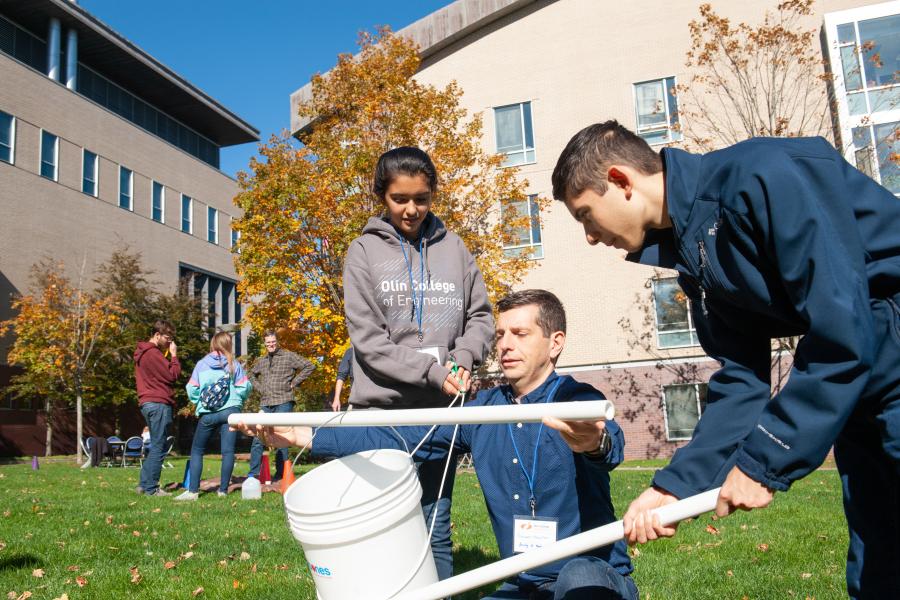 Three people outside working together to build something out of of plastic poles and a bucket