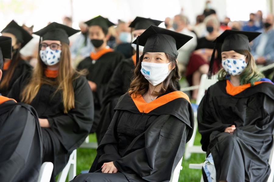 A photo of a group of student sitting in white chairs under a tent