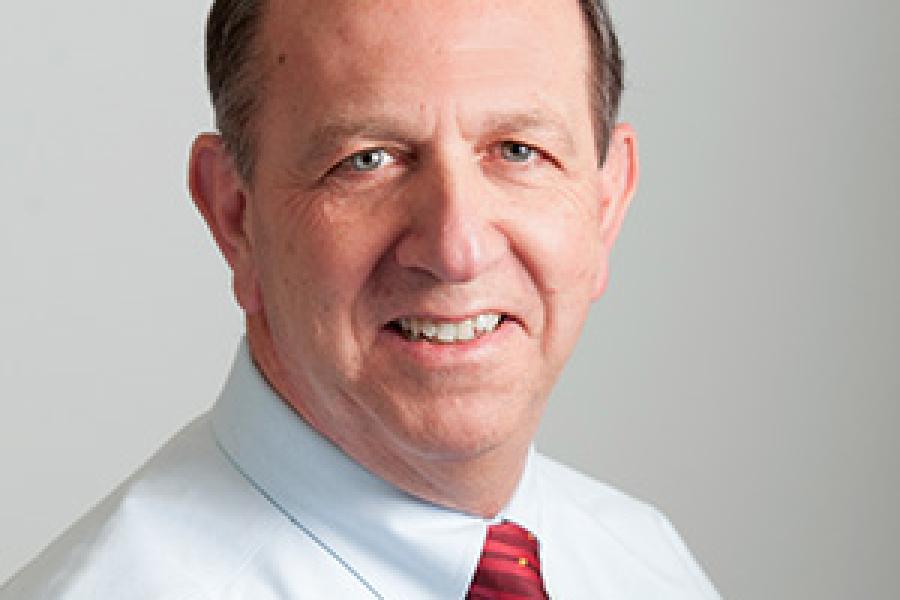 VIncent Manno wearing a white shirt with a red tie as he smiles for the camera