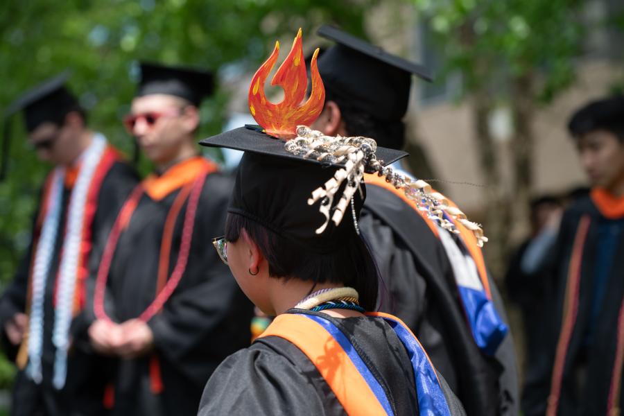 Commencement 2025 Commencement 2025, students in cap and gowns. Students fire decorated hat.