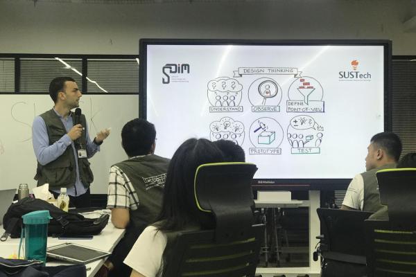 Students sit in a classroom looking at a professor standing beside a screen with an image on it