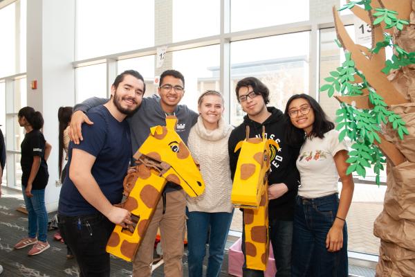 A photo of five students holding a large giraffe toy