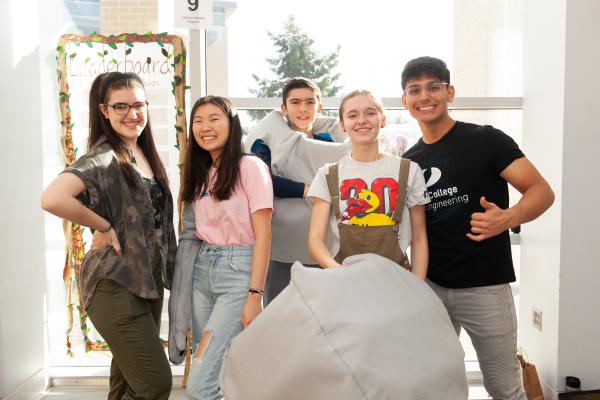 A photo of five students standing behind a medium sized white rock