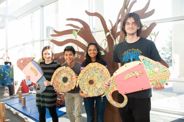 A photo of four students standing in a row each holding a piece of a chameleon toy they built
