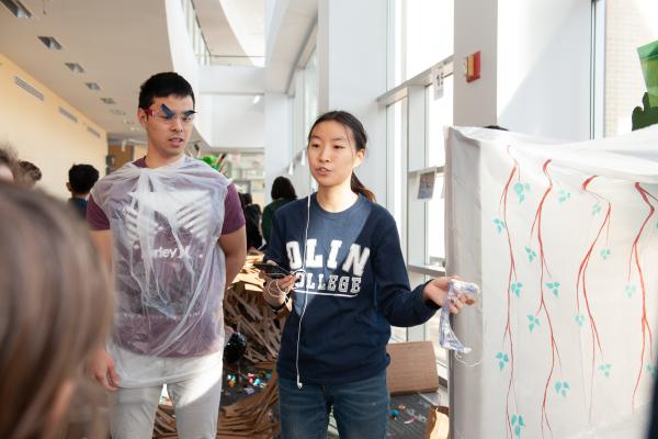 A photo of two students standing next to web that they built and are explaining to children