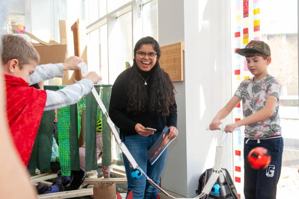 A photo of a college student explaining a toy to two fifth graders