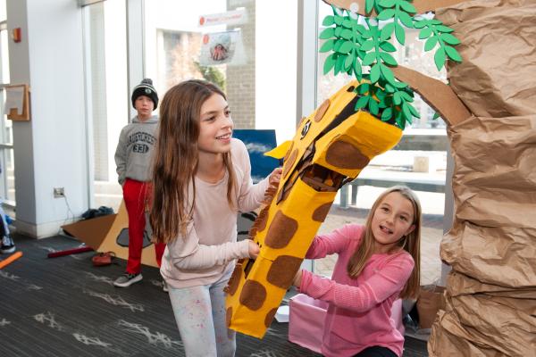 A photo of two young girls playing a game with a giraffe neck and head