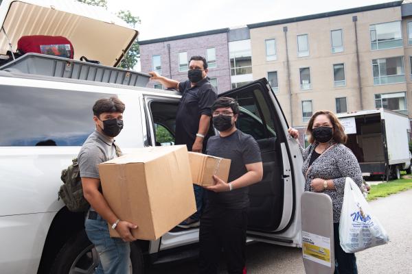 A photo of a young man and his parents unpacking their car