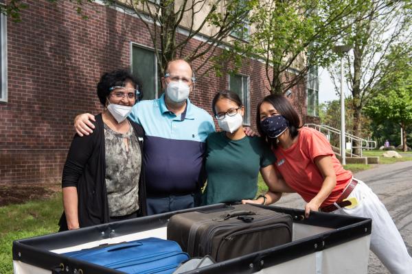 A photo of four people posing in front of a large move-in bin at college