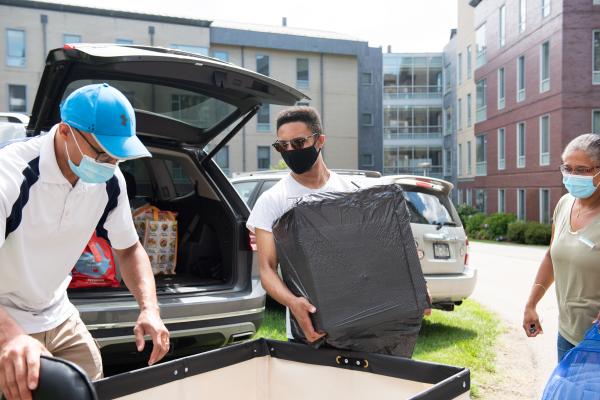 A photo of three people unpacking a car trunk