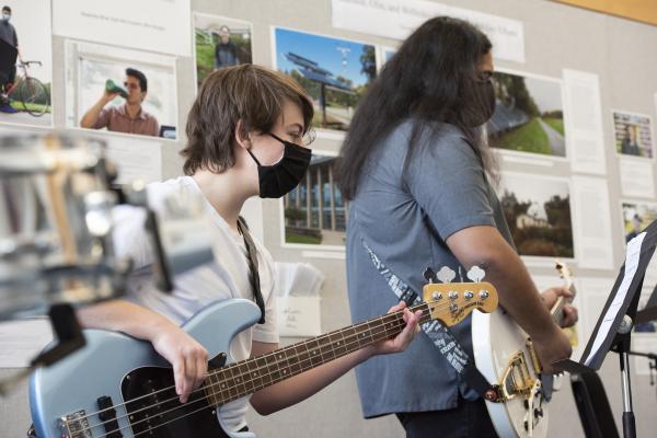 Two students play instruments, one a blue bass and the other a white guitar. 