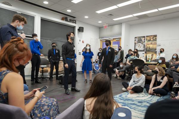 A group of students dressed in royal blue and black clothing perform a song in front of a class of students.