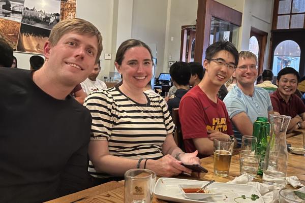 Five people look to the camera while seated next to each other at a wooden table.