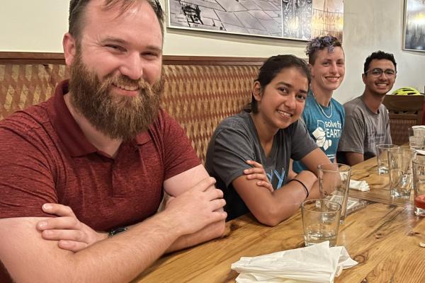 Four people smile while sitting next to each other at a wooden table.