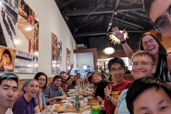 A group of people sit and stand around a dinner table.