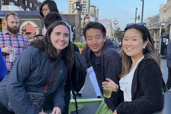 Three people lean in around green Adirondack chairs at an outside gathering.