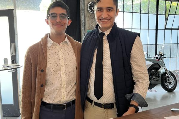 Two brothers, one with a tie, stand next to a table with plates on it.