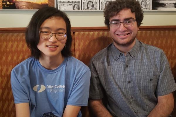 Two Oliners site in a brown booth at a restaurant. 