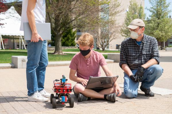 A professor watches as a student demos his robot.