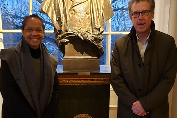 A woman stands to the left of a bronze statue and a man stands to its right