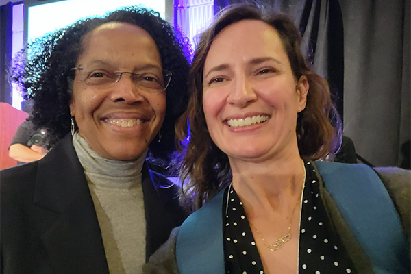 Two women standing next to one another smiling