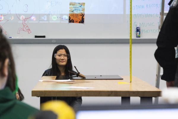 A student crouches down behind a table with a hopper device on it.
