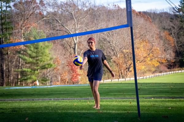 A student in a black shirt and shorts serves a volley ball on campus.