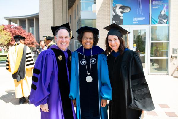 Three people stand side by side wearing academic regalia
