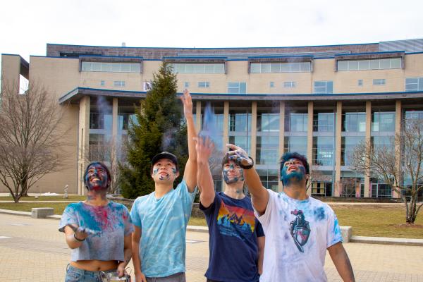 Four students throw Galal (colored powder) in the air during an on campus Holi celebration.