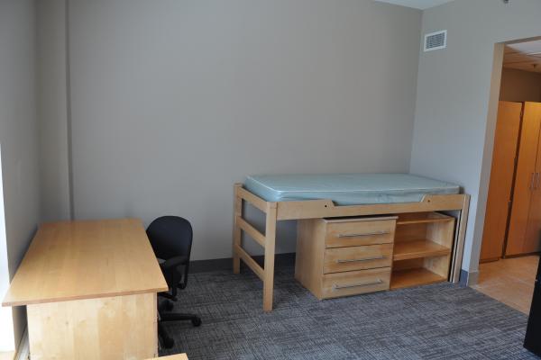 View of bed with under bed dresser and bookshelf next to desk