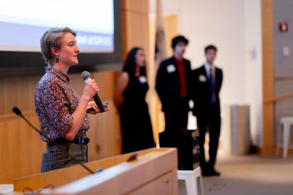 Student in foreground with microphone presenting while team is lined up in background