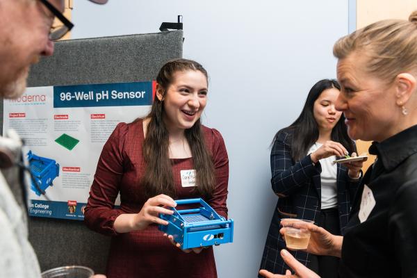 Female student holding component of SCOPE project while chatting with visitors