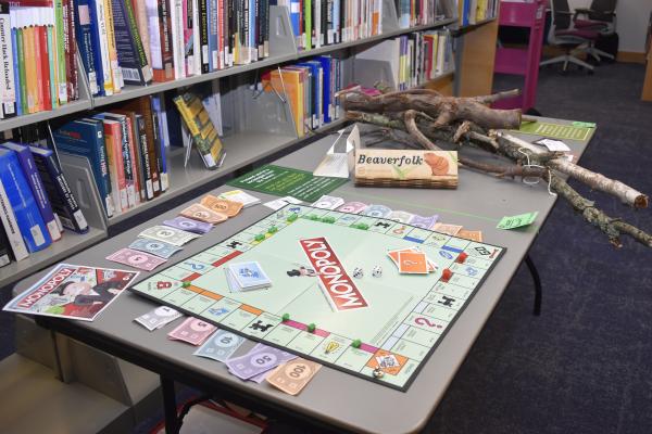A Monopoly board game sits on a table with sticks. Between the two is a sign that reads "Beaverfolk."