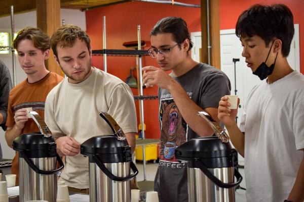 Students trying coffee at Wavelength. There are three airpots with coffee in the photo.