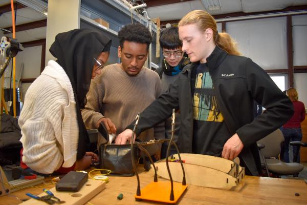 Four Olin AERO project team students collaborate with project parts  at a workbench.