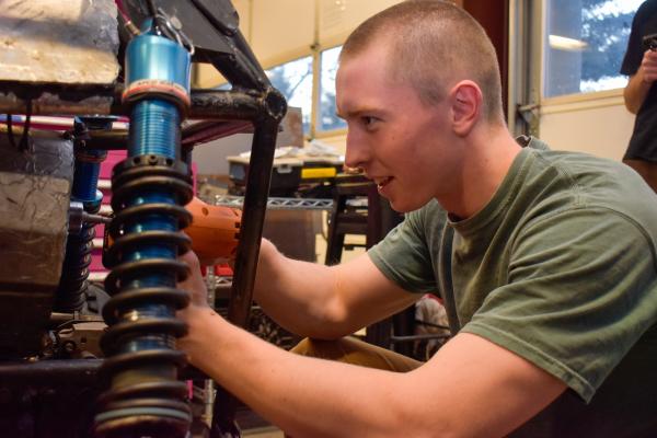 An Olin Baja project team student crouches and works on the car's suspension in the LPB.