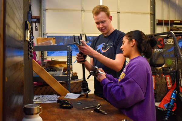 Two Olin Baja project team students collaborate with parts at a workbench.