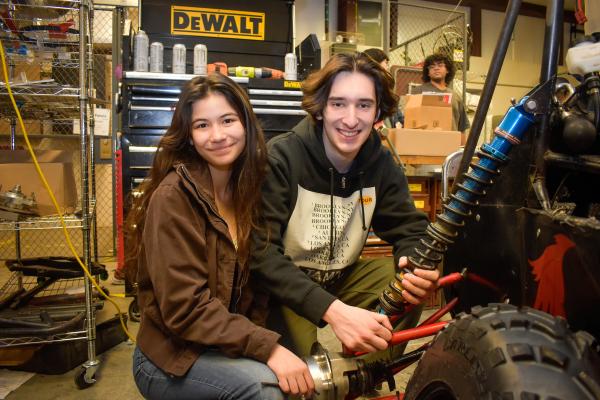 Two Olin Baja project team students pose and smile as they work on the vehicle.