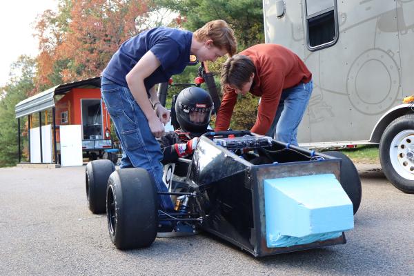 Two Olin OEM members leaning over one of their cars with a teammate sitting in it.