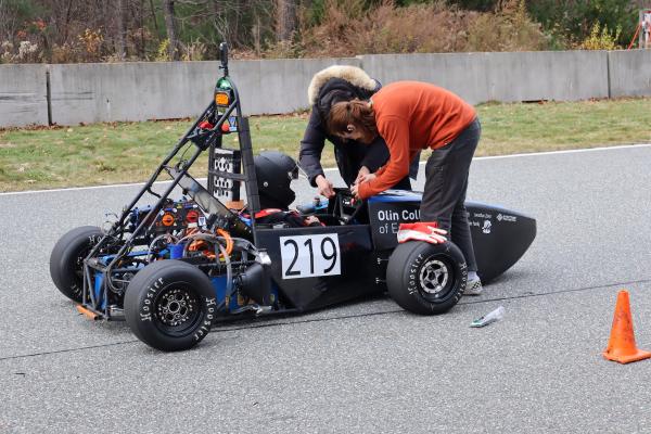 Two Olin OEM members leaning over one of their cars with a teammate sitting in it.