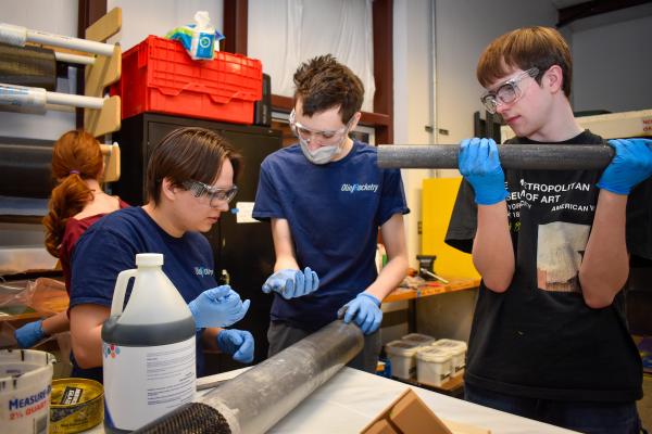 Three Olin Rocketry project team members work together at a workbench.
