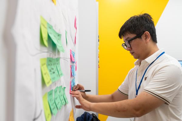 A Summer Studio 2025 participant writes on a sticky note that's pasted to a wall poster.