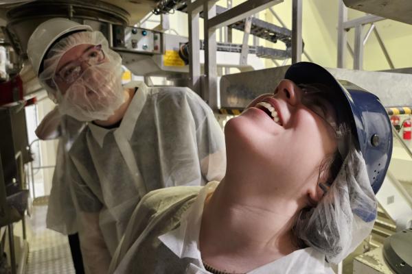 Two students looking up into a machine. 