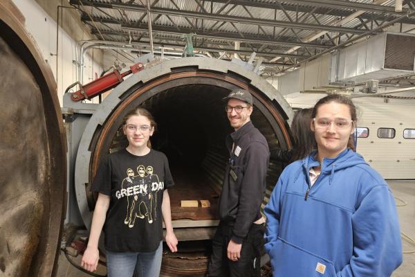 Coby and two students pose in front of a machine at The Moore Brothers Company. 