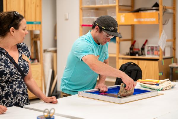 Dyllan Nguyen assists a Makerspace Institute participant with their screen printing. 